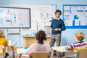 Elementary School Physics Teacher Uses Interactive Digital Whiteboard to Show to a Classroom full of Smart Diverse Children how Renewable Energy Works. Science Class with Kids Listening